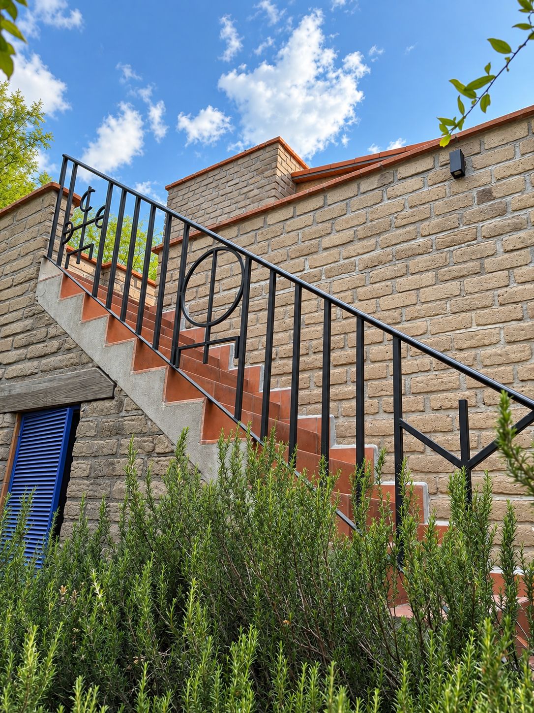 Eine Wendeltreppe mit Metallgeländer führt zu einem Backsteinhaus mit einem Fenster mit blauen Fensterläden.