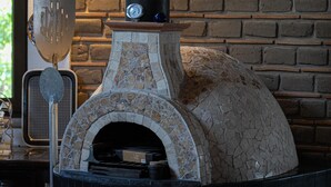 Ein Backofen aus Ziegelsteinen mit Schornstein, ein Metallspatel und ein Thermometer auf einer Arbeitsfläche.