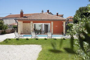 Ein Haus mit Swimmingpool, Sitzgelegenheiten im Freien und einer Steinmauer.