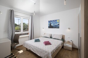 Une chambre à coucher avec un lit, une chaise, une table de chevet, un tableau et une fenêtre avec des rideaux.