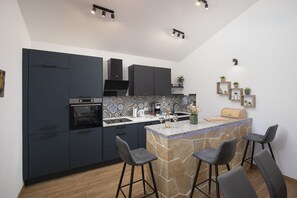 Eine moderne Küche mit dunklen Schränken, einem eingebauten Backofen, einer Stein-Kochinsel mit Barhocker und einer gefliesten Spritzschutzwand.