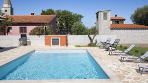 Una piscina con sdraio, un barbecue e un muro in pietra.