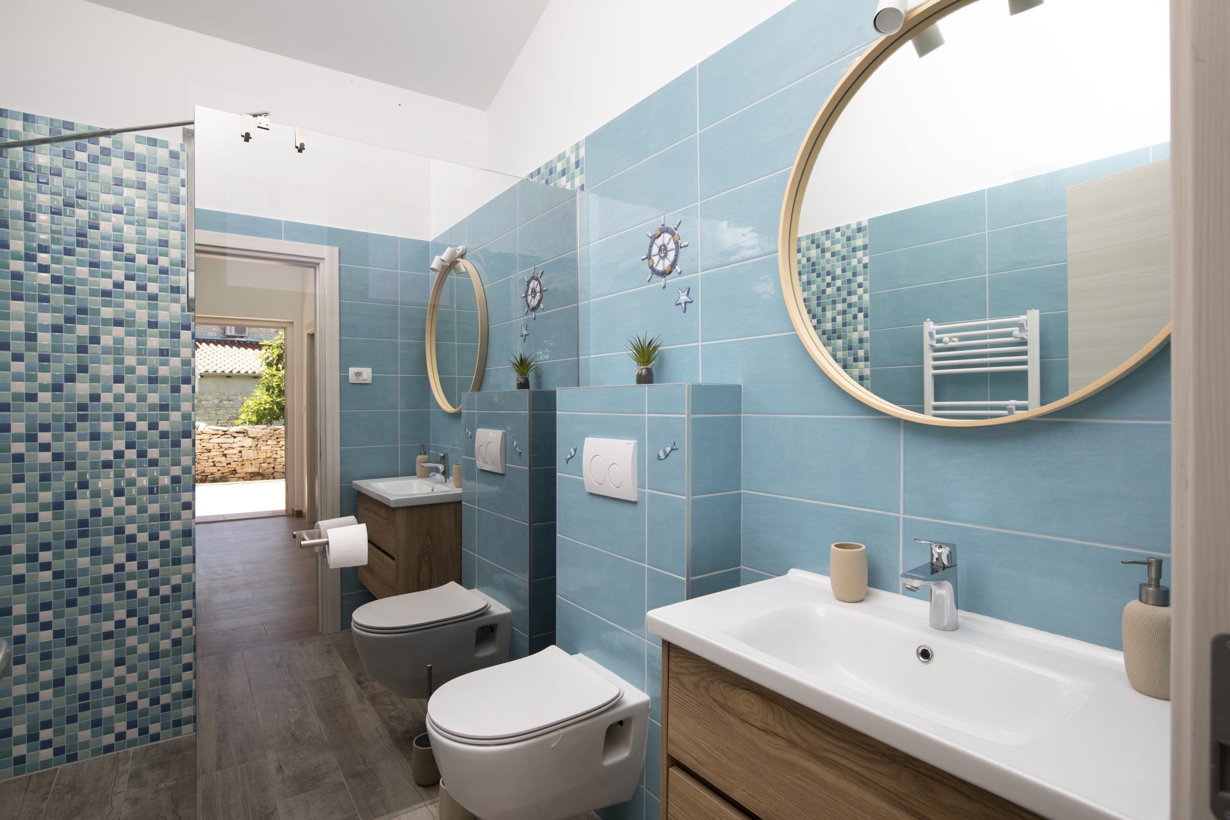 A bathroom with blue tiles, two toilets, a sink, and a mirror.