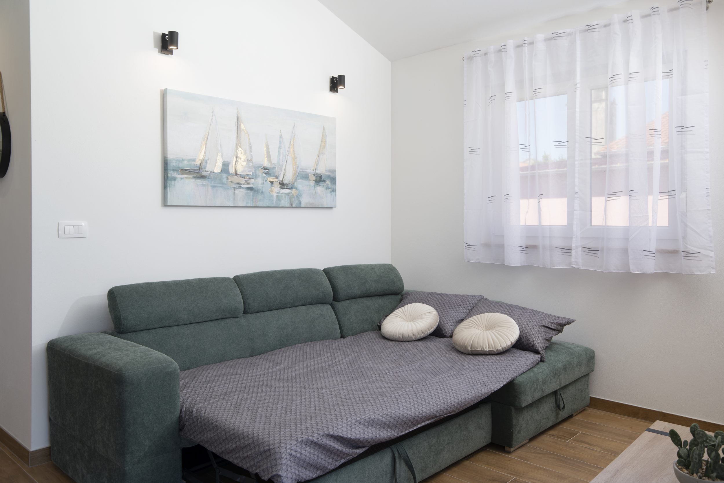 Ein modernes Wohnzimmer mit einem grünen Sofa, einer grauen Decke und einem Gemälde eines Segelboots an der Wand.