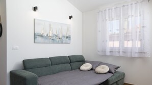 Un soggiorno moderno con un divano verde, una coperta grigia e un quadro raffigurante una barca a vela.