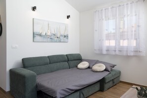 Ein modernes Wohnzimmer mit einem grünen Sofa, einer grauen Decke und einem Gemälde eines Segelboots an der Wand.