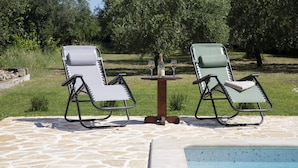 Due poltrone con un tavolino e una bottiglia di vino, posizionate su un patio in pietra con una piscina sullo sfondo.