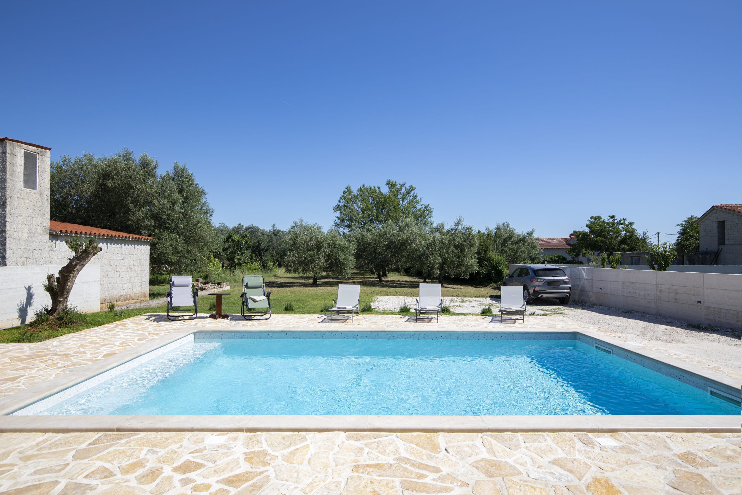 Una piscina con sillones de descanso y un deck con baldosas de piedra.