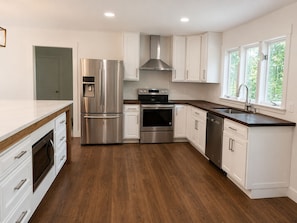 Una cocina moderna con electrodomésticos de acero inoxidable, armarios blancos y piso de madera.