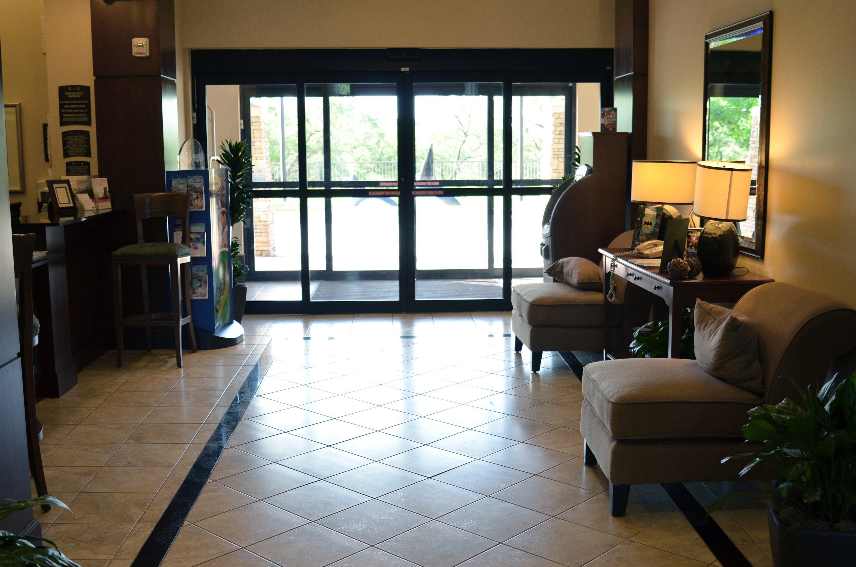 A hotel lobby with a reception desk, a seating area with a sofa and armchairs, a coffee table, and a large window with a view of the outdoors.