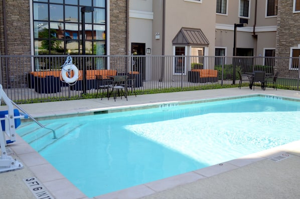 En swimmingpool med en livboj, utomhusmöbler och en byggnad med en fasad av sten och tegel i bakgrunden.