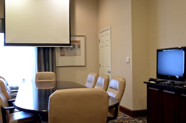 A conference room with a large table, four chairs, a projector screen, a television, and a door.
