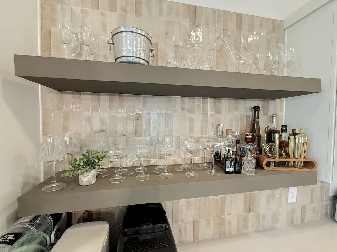 A kitchen with a countertop holding wine glasses and bottles, a plant, and a coffee machine.