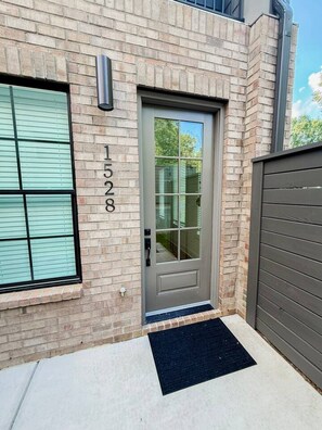 A residential building with a brick facade, a grey door, and a mailbox on the wall. - Luxury Designer Home | Steps to NoDa | City Views (Charlotte)