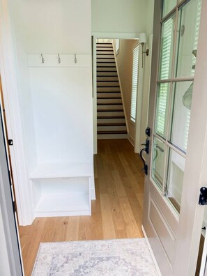 A hallway with a wooden floor, a white door with glass panels, and a staircase in the background. - Luxury Designer Home | Steps to NoDa | City Views (Charlotte)