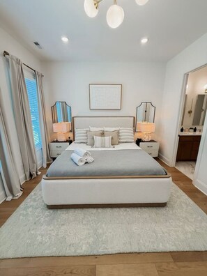A bedroom with a large bed, bedside tables, a mirror, and a window with curtains. - Luxury Designer Home | Steps to NoDa | City Views (Charlotte)