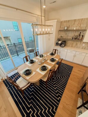 A dining area with a table set for six, a chandelier, and a kitchen area with cabinets and appliances. - Luxury Designer Home | Steps to NoDa | City Views (Charlotte)