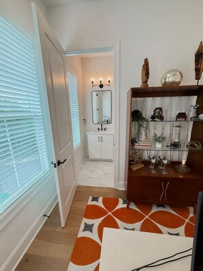 A hallway with a white door, a mirror, and a shelf with decorative items. - Luxury Designer Home | Steps to NoDa | City Views (Charlotte)