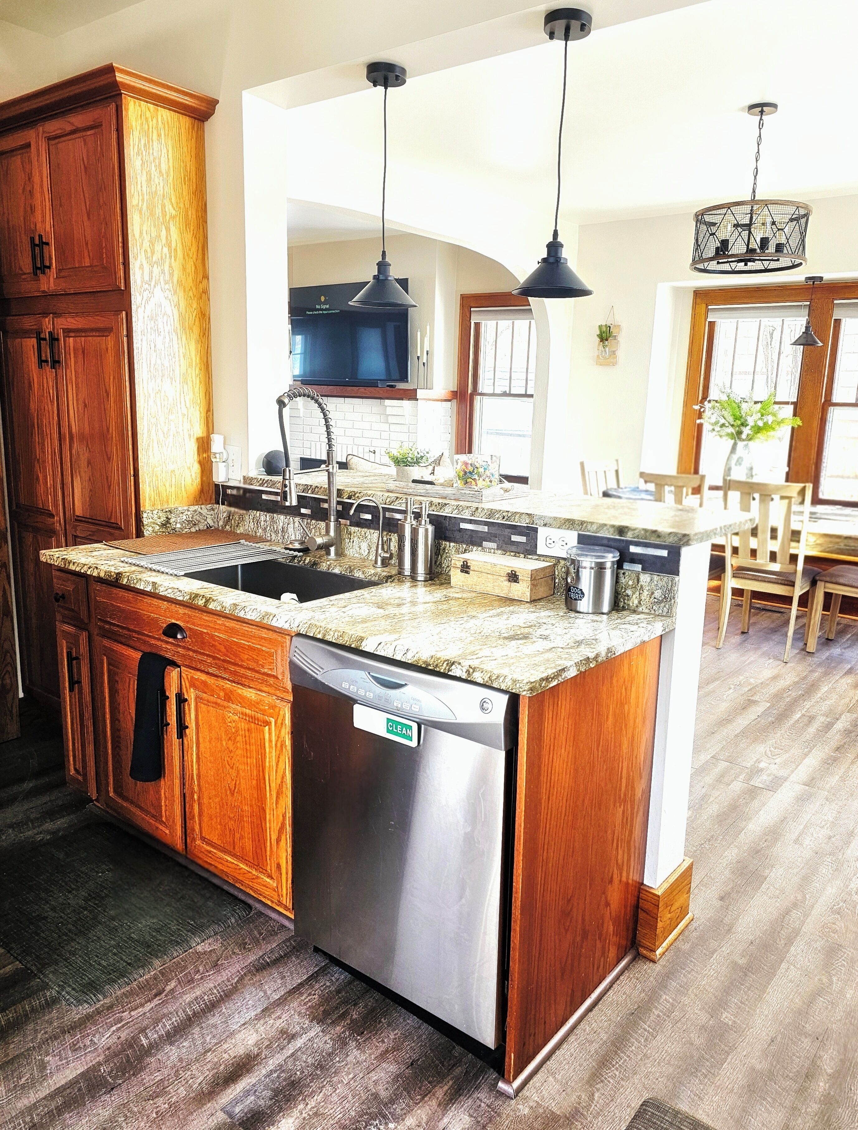 Une cuisine dotée de meubles en bois, d’un lave-vaisselle en acier inoxydable, d’un comptoir en granit et de luminaires suspendus.