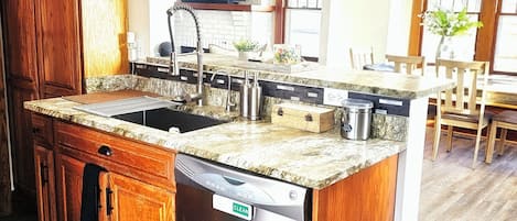 A kitchen with wooden cabinets, a stainless steel dishwasher, a granite countertop, and pendant lighting.