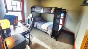 A compact room with a bunk bed, a desk with a computer, and a chair.
