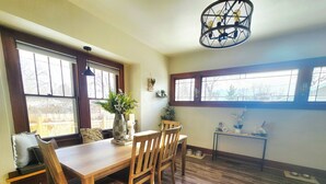 A dining area with a wooden table and chairs, a vase with flowers, and a hanging light fixture.