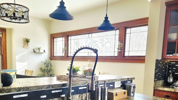 A kitchen with a large island, a double sink, pendant lighting, and a window with a view of trees.