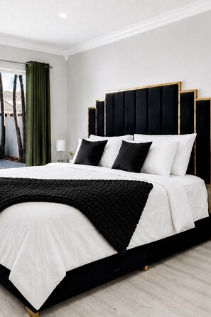 A modern bedroom with a large bed, a headboard with vertical panels, and a view of the outdoors through a window.