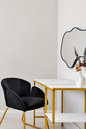 A modern room with a black upholstered chair, a white marble table, and a yellow metal frame.