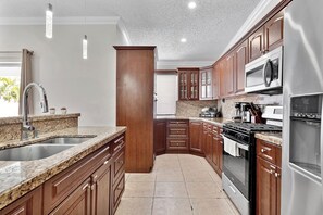 A kitchen with granite countertops, wooden cabinets, stainless steel appliances, and a granite backsplash.