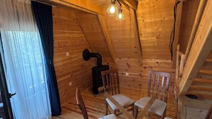 Ein gemütliches Holzhäuschen mit Esstisch, umringt von Stühlen, Kamin und einem mit Vorhängen drapierten Fenster.