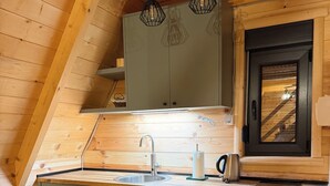Eine Küche mit Holzschränken, einem Spülbecken, einem Wasserkocher und einem Fenster mit Blick ins Innere.
