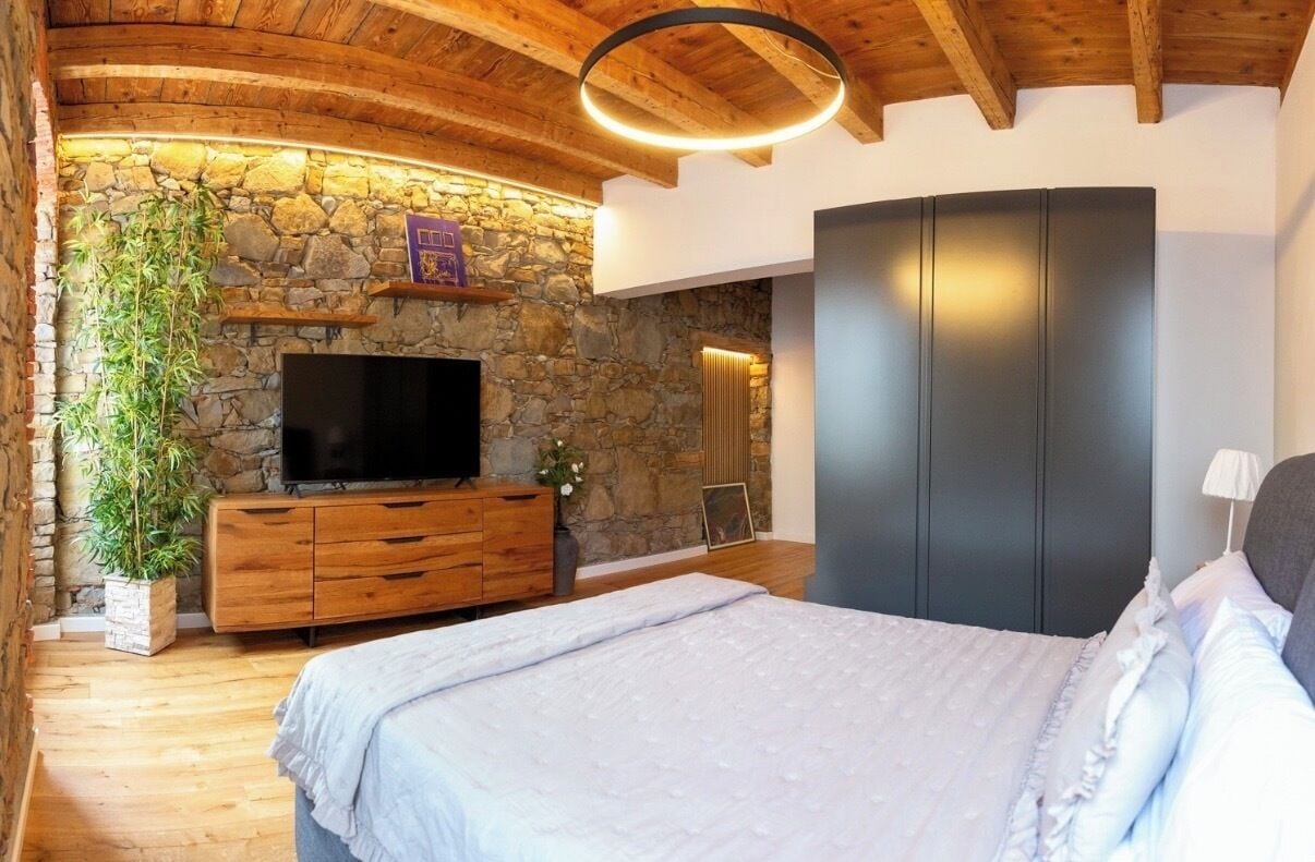 Ein Schlafzimmer mit Steinwand, Holzboden und einem Bett, einem Fernseher und einem Kleiderschrank.