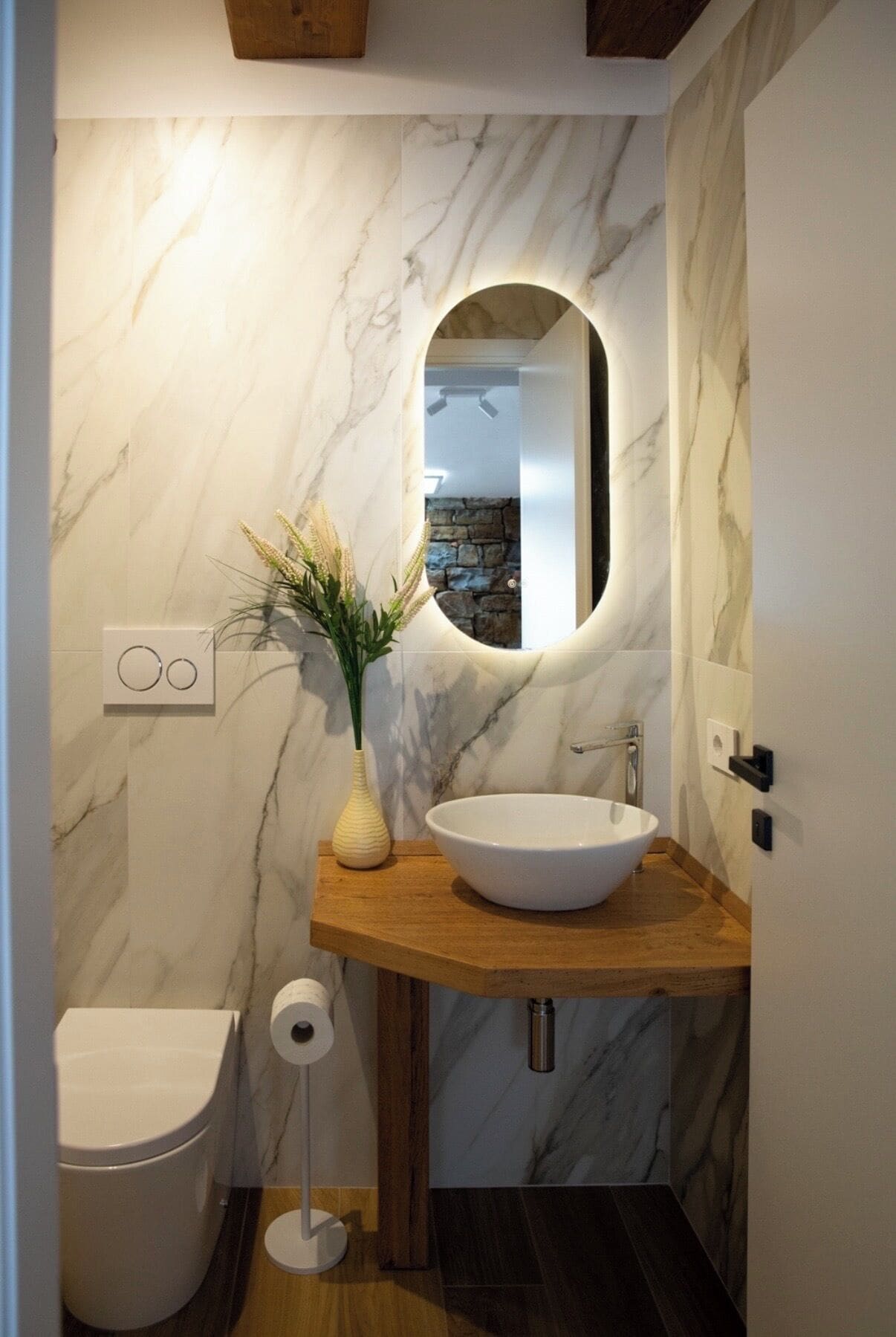 Un bagno con una parete in marmo, un mobile contenitore in legno, un lavabo bianco, un water e uno specchio.
