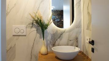Un bagno con una parete in marmo, un mobile contenitore in legno, un lavabo bianco, un water e uno specchio.