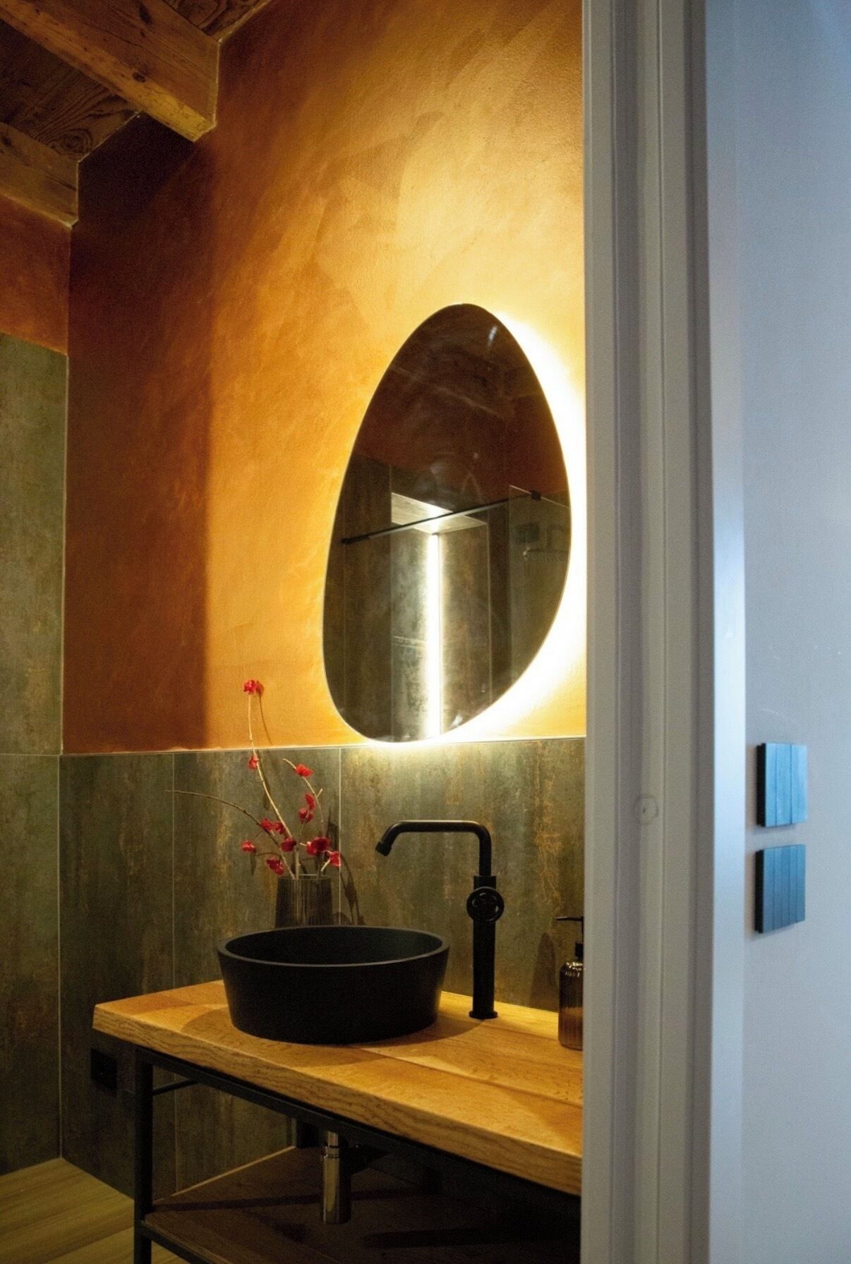 Un bagno con un mobile contenitore in legno, un lavandino nero e un ampio specchio ovale.