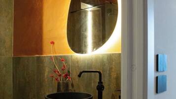 Un bagno con un mobile contenitore in legno, un lavandino nero e un ampio specchio ovale.