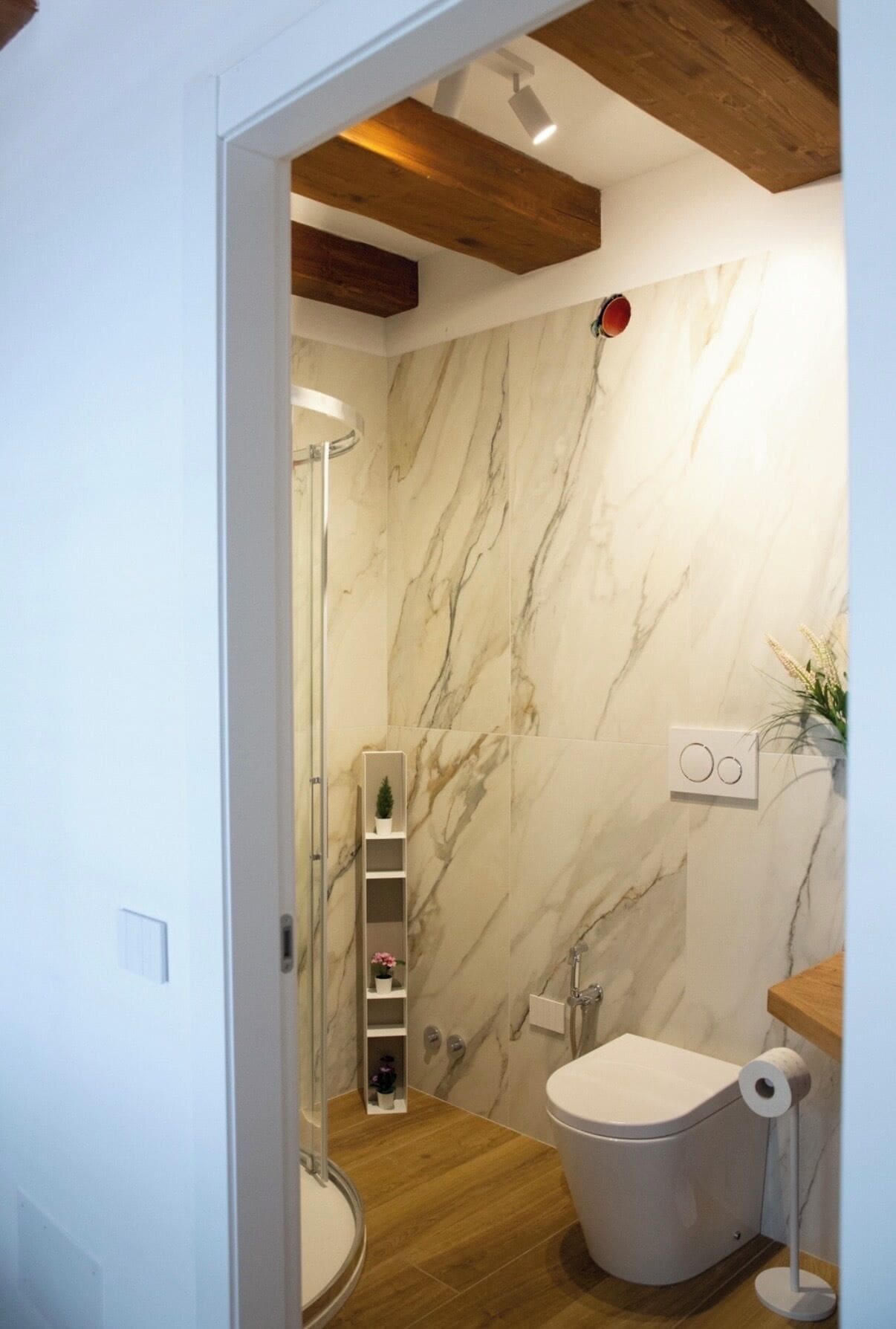 Un baño con inodoro, ducha y pared de mármol.