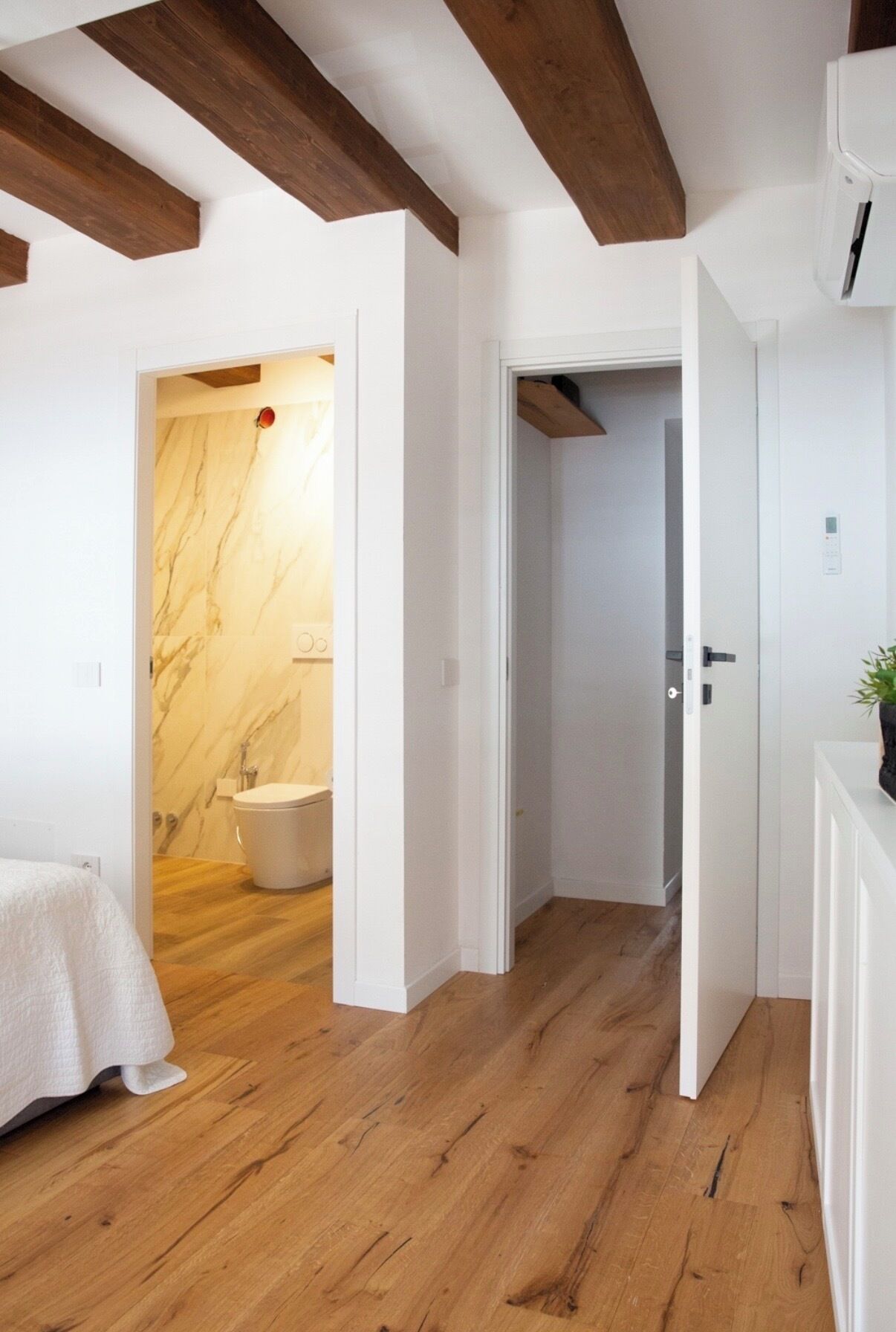 Un baño moderno con pared de mármol, suelo de madera y inodoro blanco.