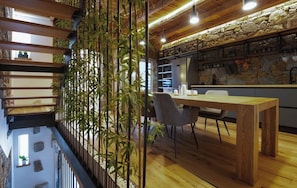 Un comedor con mesa y sillas de madera, un separador de bambú y una pared de piedra al fondo.