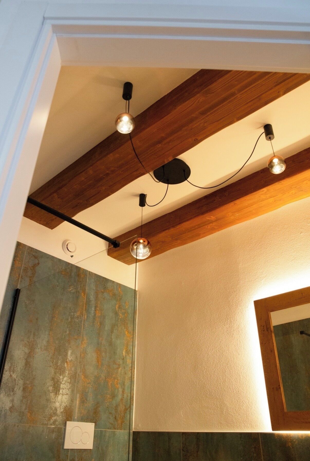 Un baño con una viga de madera en el techo, una lámpara de pared y un espejo.
