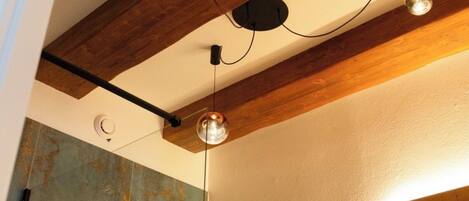 Un baño con una viga de madera en el techo, una lámpara de pared y un espejo.