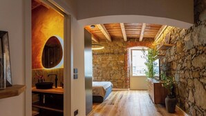 Una stanza con parete in pietra, pavimento in legno, un letto, un lavandino e una finestra.