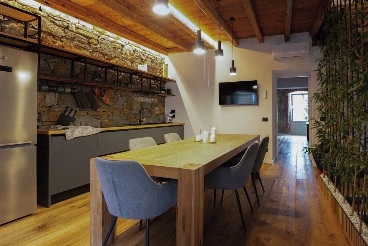 A modern kitchen with a stone wall, wooden ceiling, and a dining area with a long table and chairs.