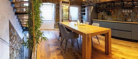 A wooden dining table with chairs, a stone wall, and a staircase.