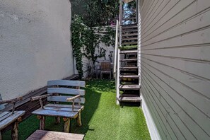 A narrow outdoor area with a wooden bench and a small table, a grassy patch, and a metal staircase leading up to a building. - Bright 2BR Home with Private Garden and Free Parking (Herzliya)