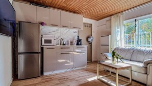 Una cocina moderna con horno empotrado, microondas y refrigerador. Cuenta con techo de madera y una ventana con vista a zonas verdes.