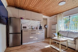 A modern kitchen with a built-in oven, microwave, and refrigerator. There is a wooden ceiling and a window with a view of greenery outside. - Bright 2BR Home with Private Garden and Free Parking (Herzliya)