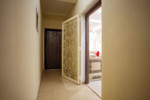 A hallway with a dark wooden door, a decorative white door frame, and a tiled floor. - Authentic Moroccan Apt 2BR 8 min Airport AC and Parking Marrakech (Marrakech)