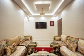 A living room with two sofas, a TV, a chandelier, and a red carpet. - Authentic Moroccan Apt 2BR 8 min Airport AC and Parking Marrakech (Marrakech)